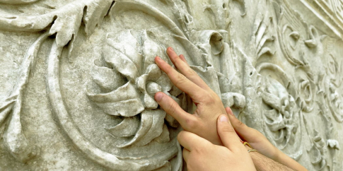 Mani che toccano una decorazione vegetale dell’Ara Pacis